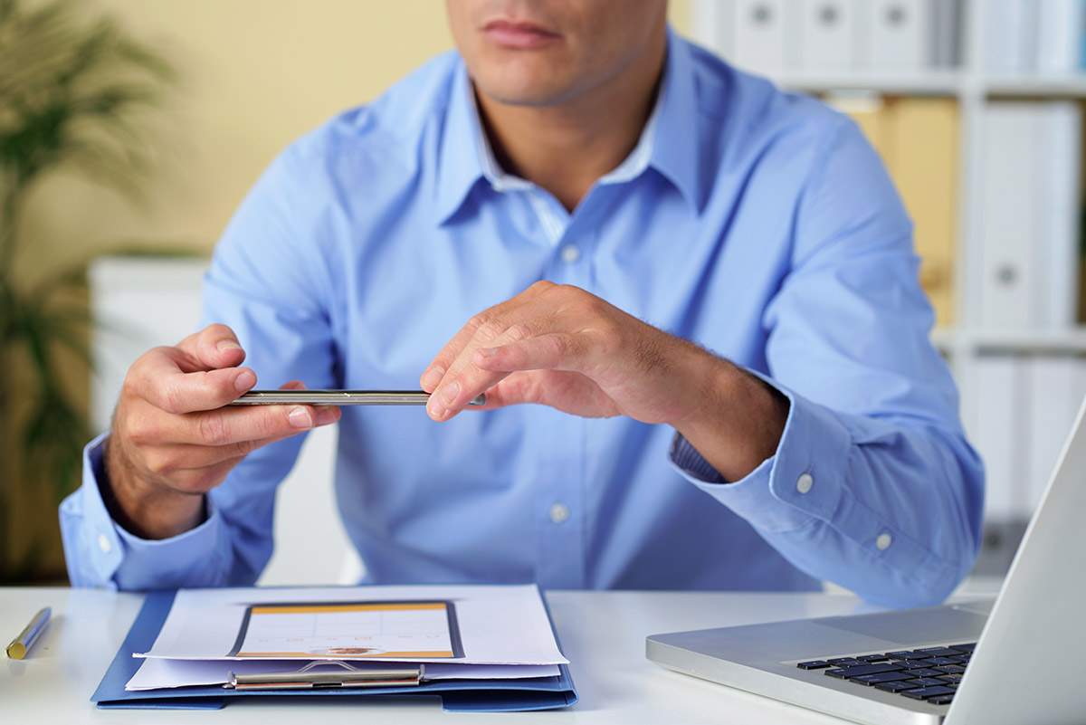 Businessman using smartpone to take photo of document on his table